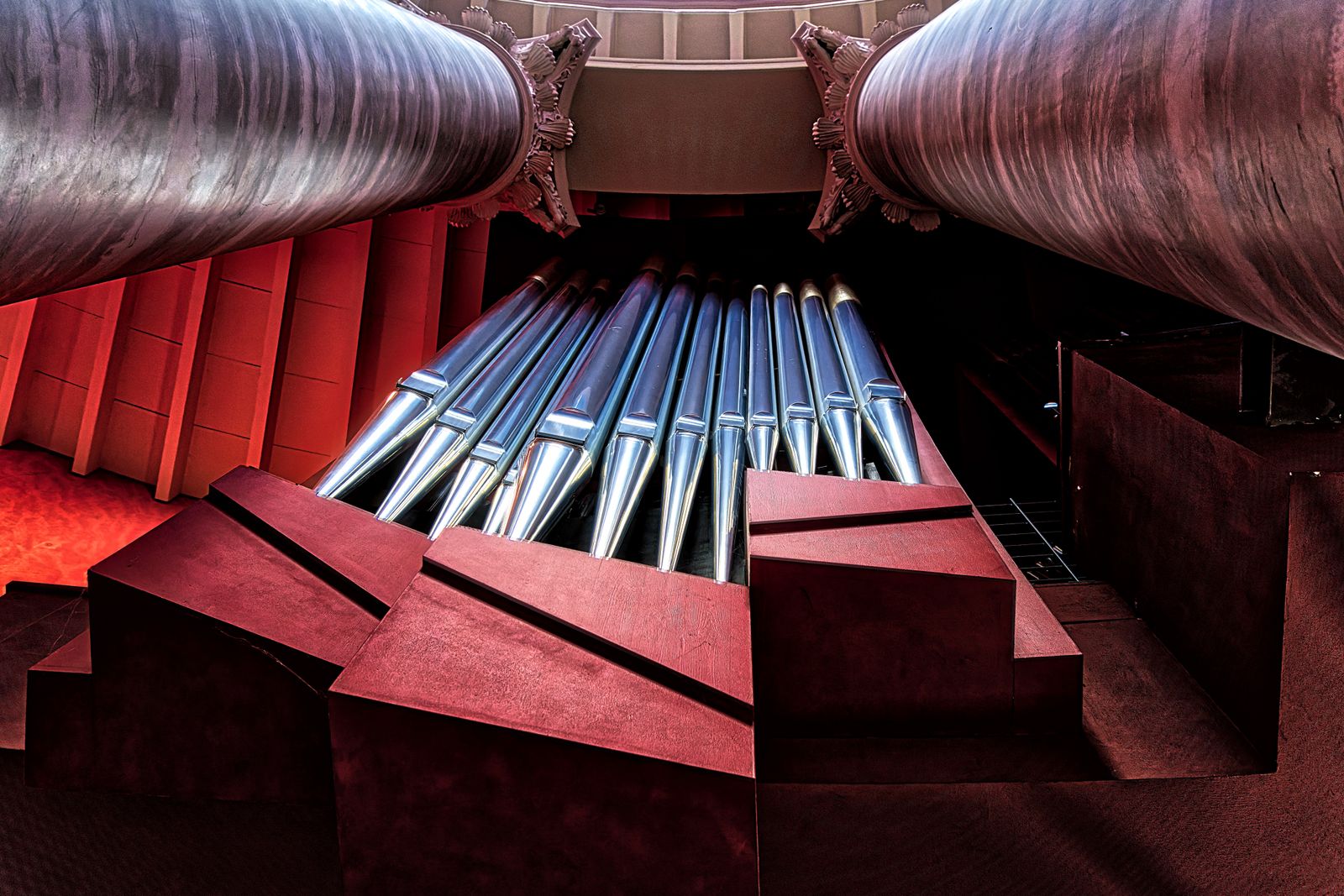 Dramatic view of pipe organ pipes lit red inside a hall