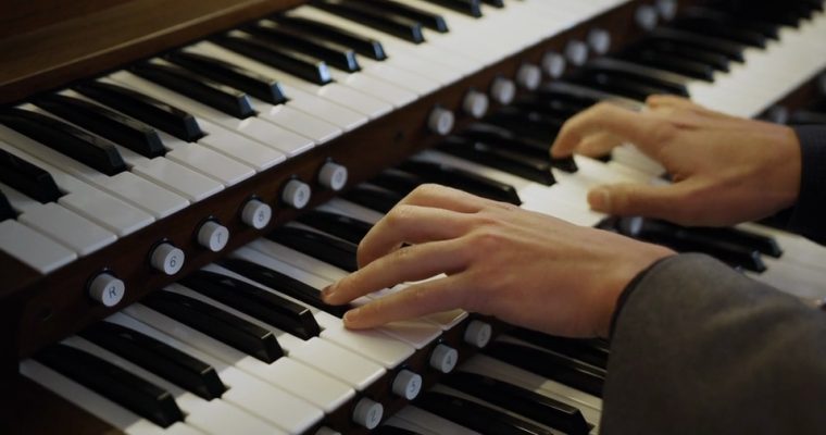 Hands playing a pipe organ console across two manuals